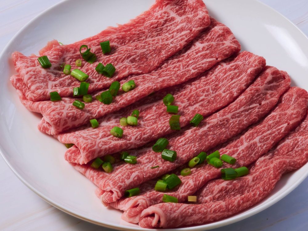 白い皿に並べた薄切りの黒毛和牛と刻みねぎ
